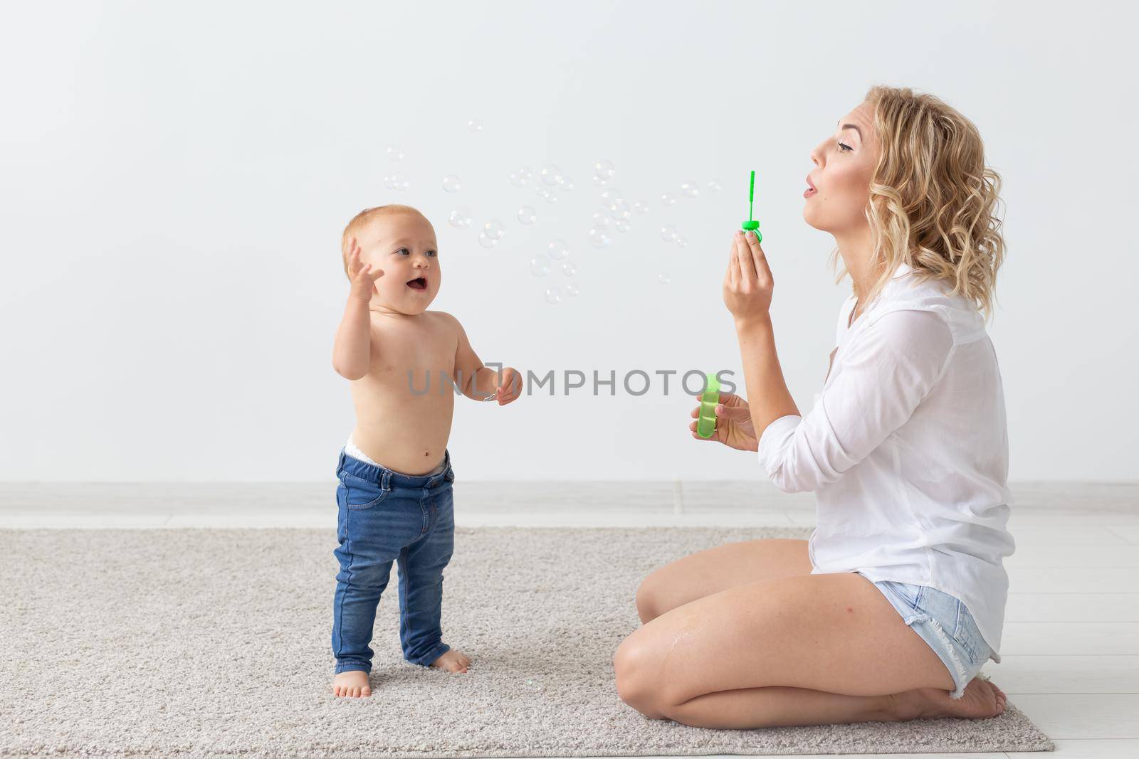 Family and parenting concept - Cute baby playing with her mother on beige carpet.