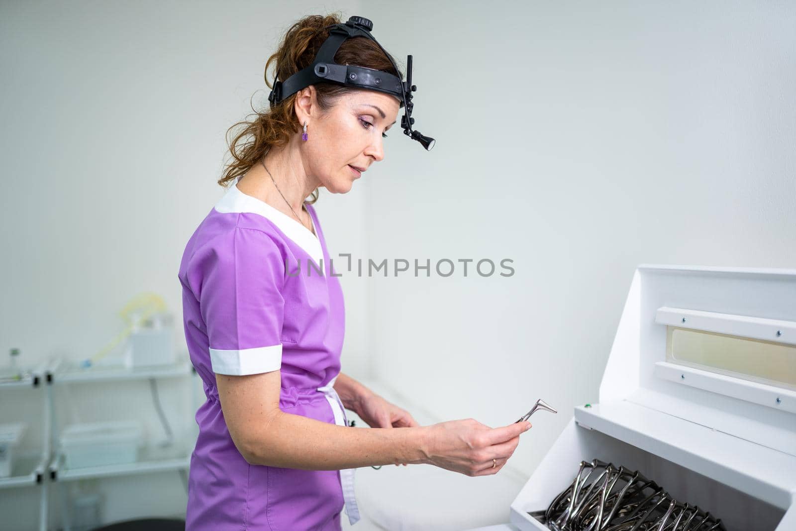 Profession medical industry. Portrait of woman ENT doctor posing in office before examining patient. Physician in bright colored uniform with medical equipment and tools for ENT practice in hospital by Tomashevska