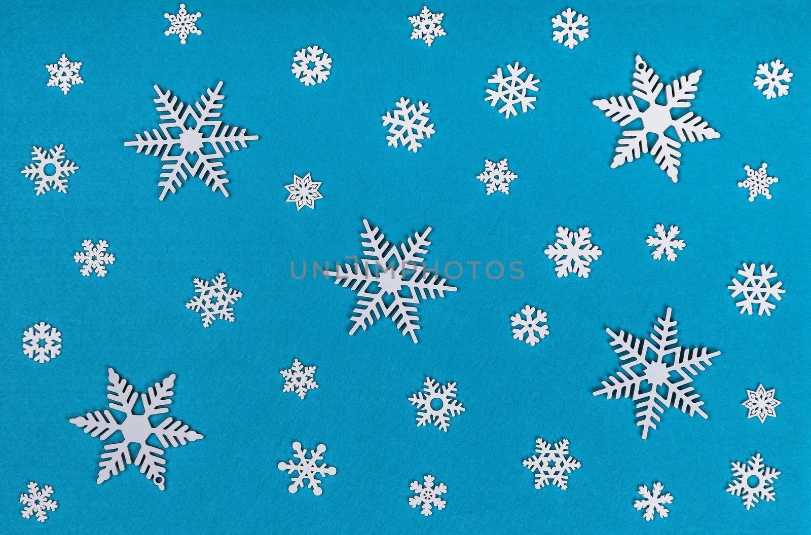 Close up pattern of white wooden snowflakes Christmas decoration over blue felt background, table top view, flat lay