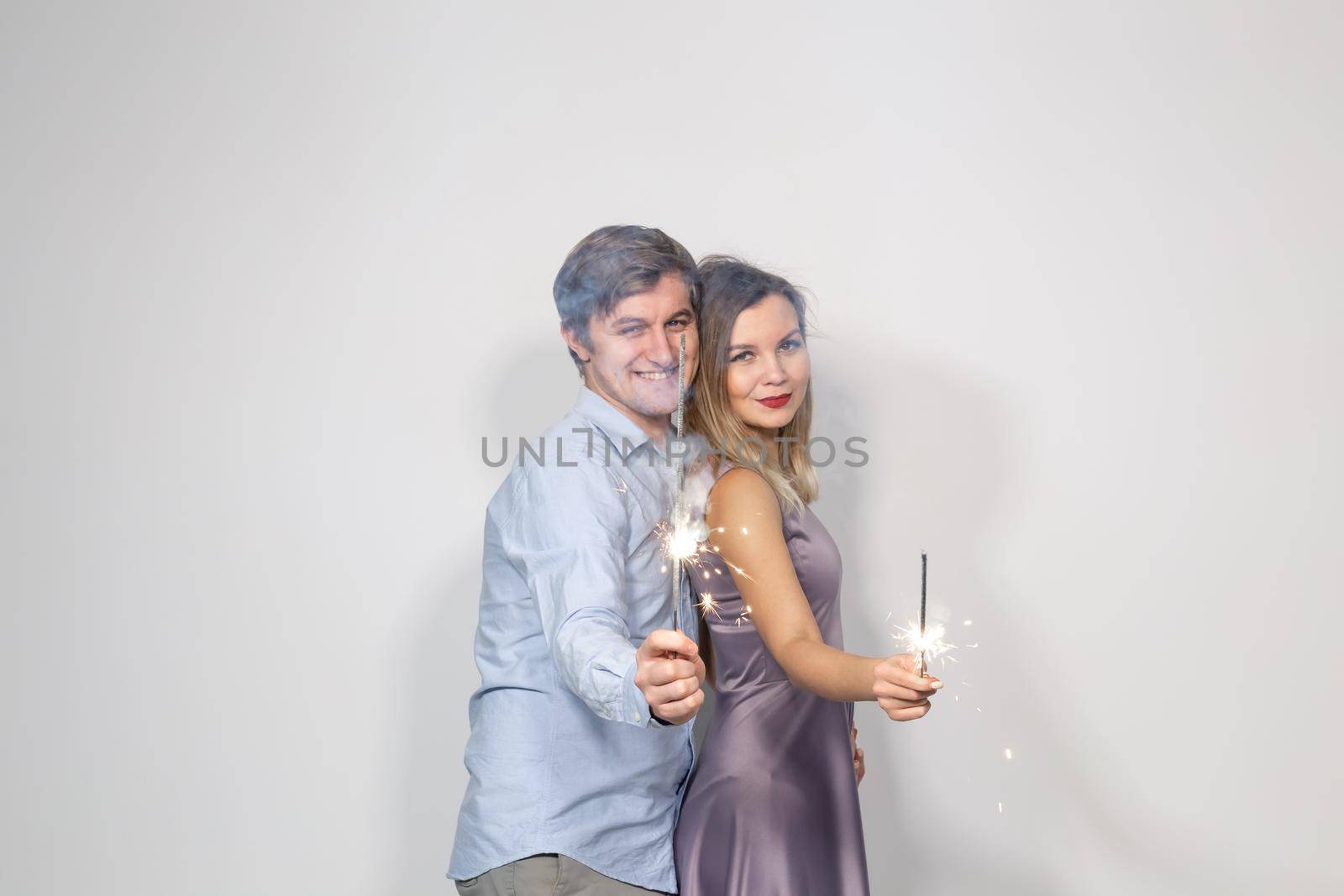 Holidays, party and celebrations concept - young couple with sparklers on white background.