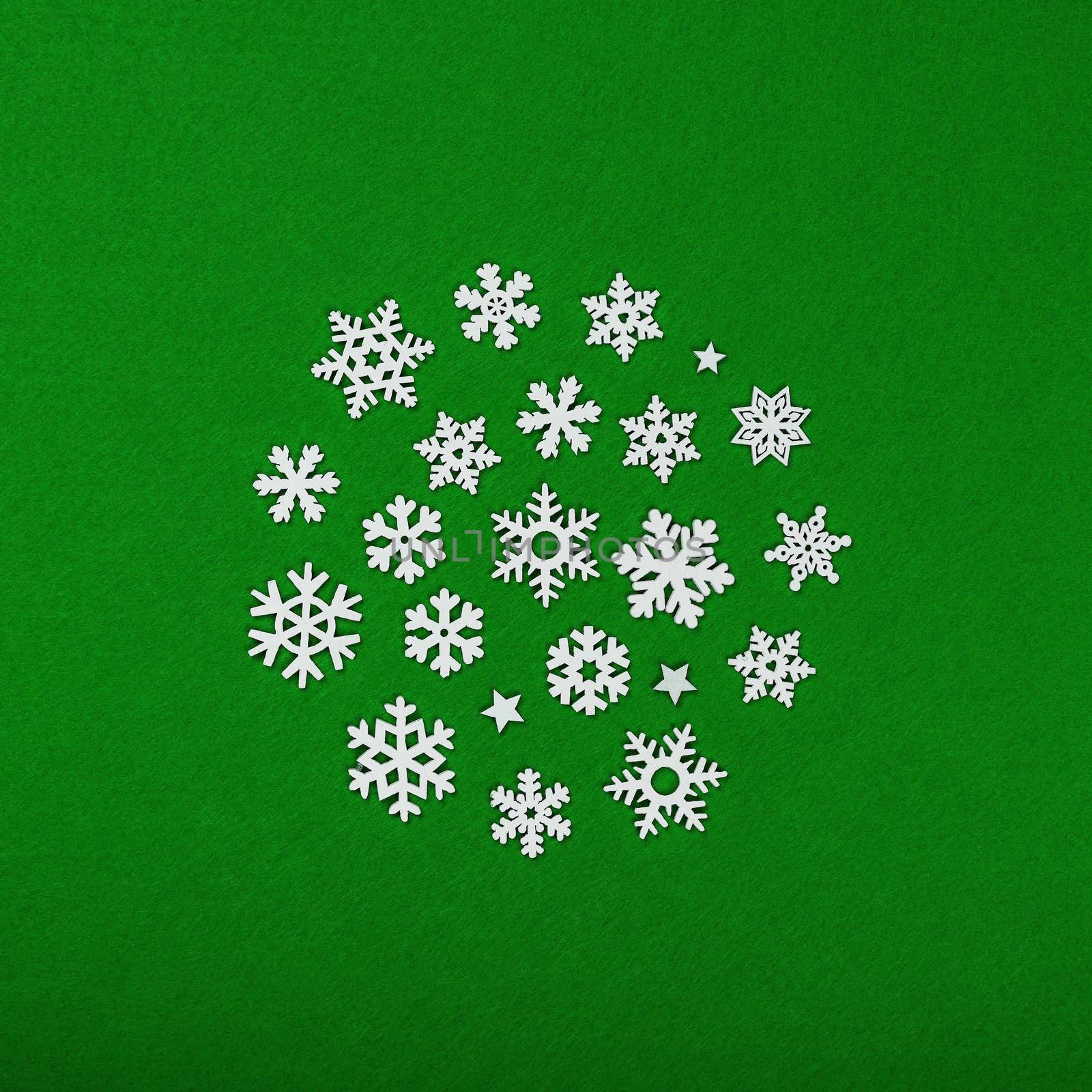 Close up circle of white wooden snowflakes Christmas decoration over green felt background, table top view, flat lay