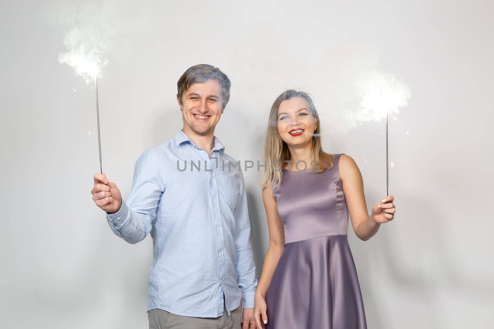 Party, celebration, event and holidays concept - man dressed in blue shirt and woman dressed in purple dress hold a firework stick.