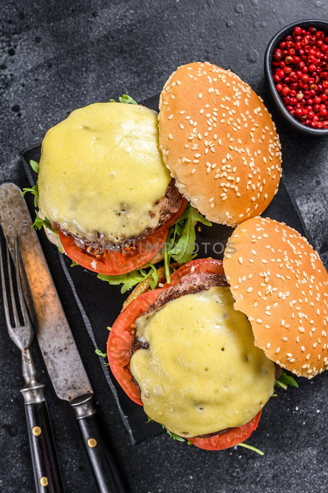 Grilled homemade burgers with beef, tomato, cheese, cucumber and lettuce. Black background. Top view.