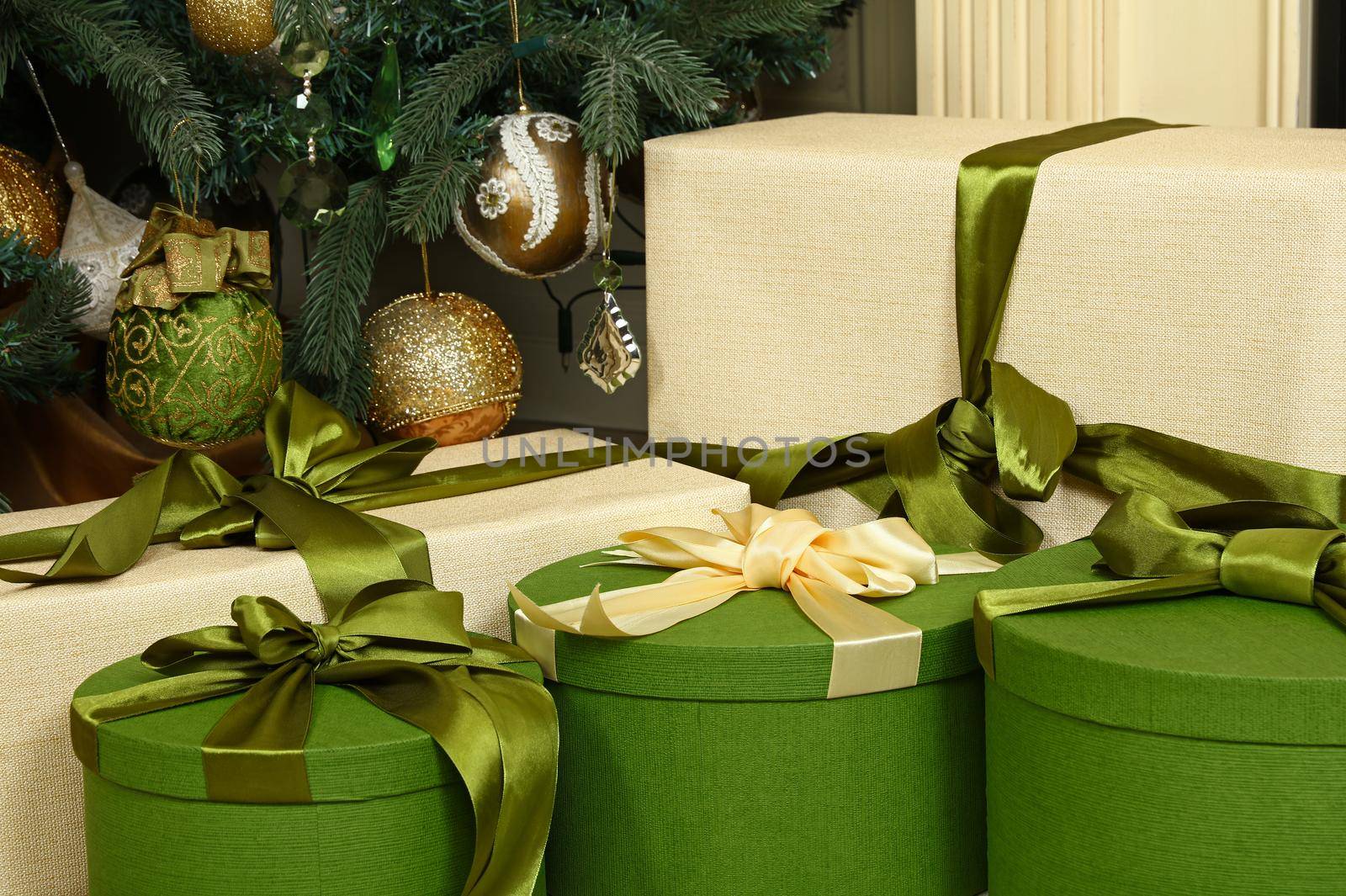 Close up green and beige paper wrapped gift boxes with ribbon bows under decorated Christmas tree, high angle front view