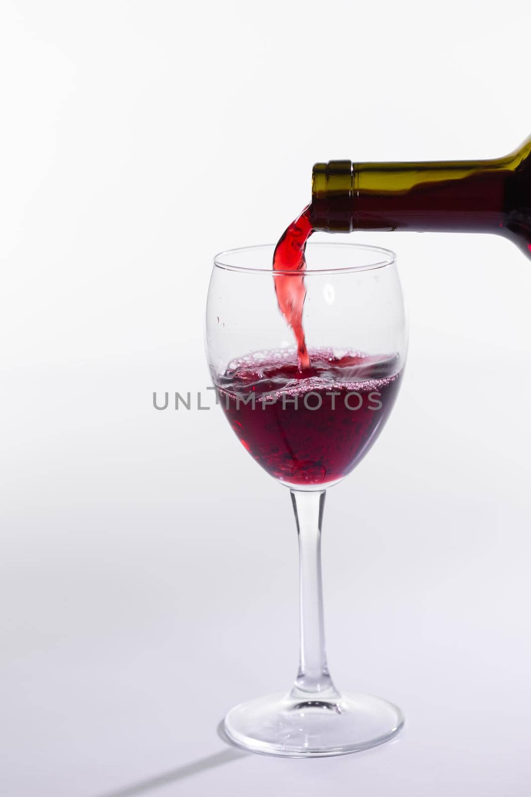 Red wine pouring into glass from bottle on white background.