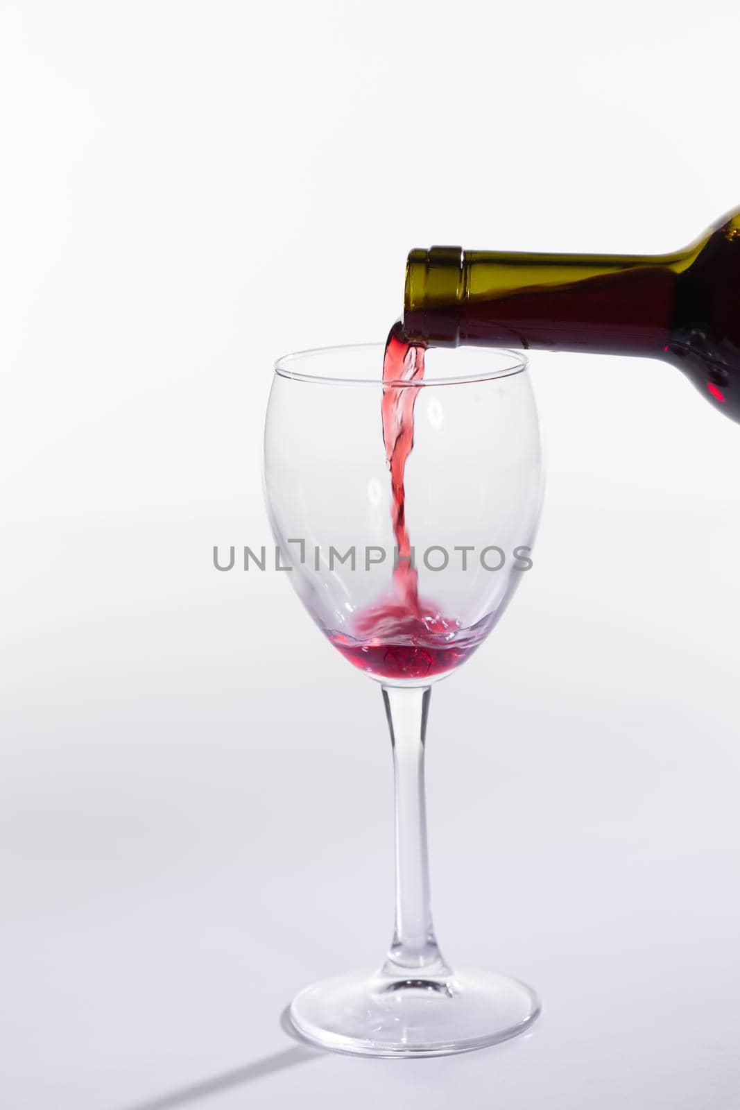 Pouring red wine into the glass on white background.