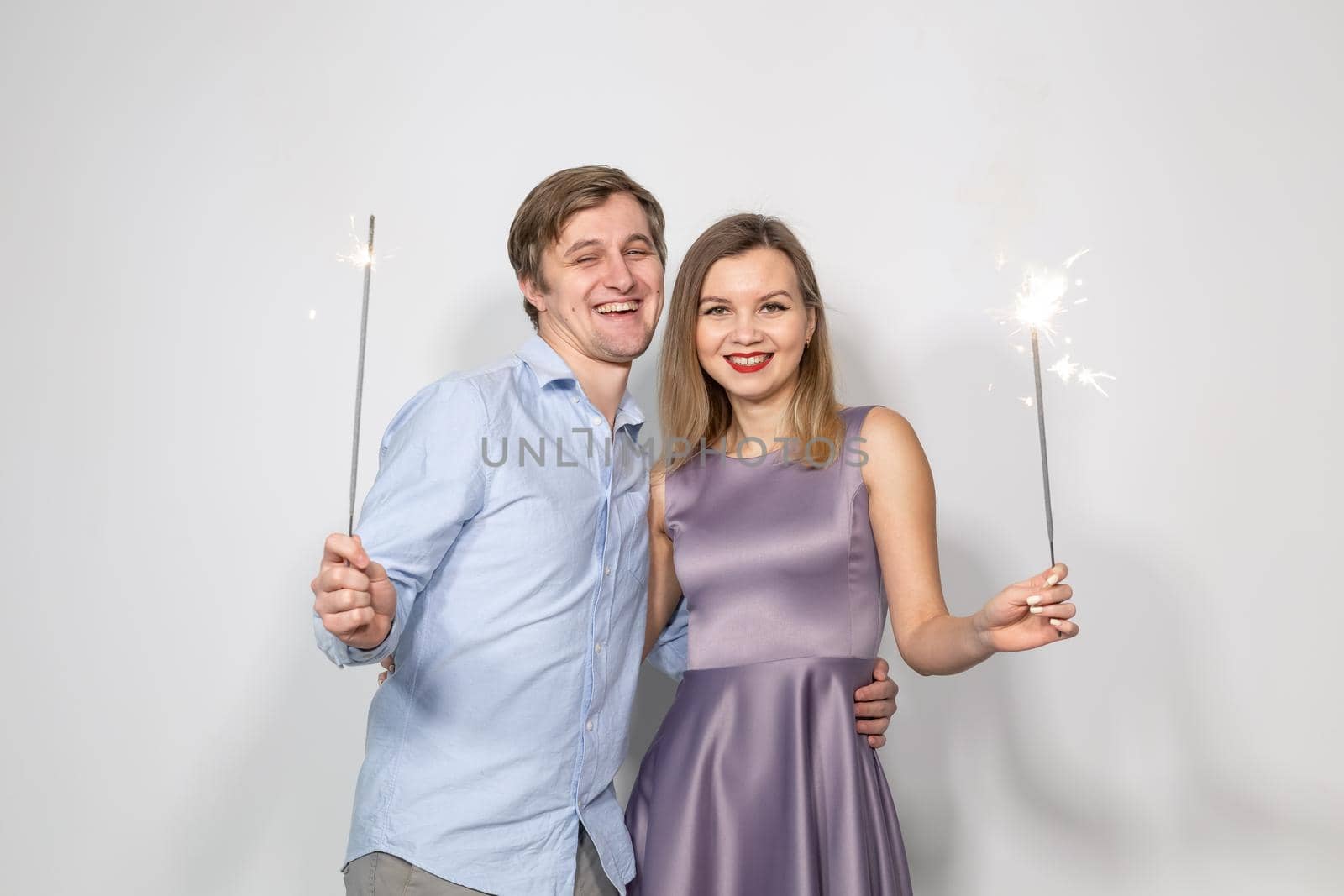 Party, celebration, event and holidays concept - man dressed in blue shirt and woman dressed in purple dress hold a firework stick.