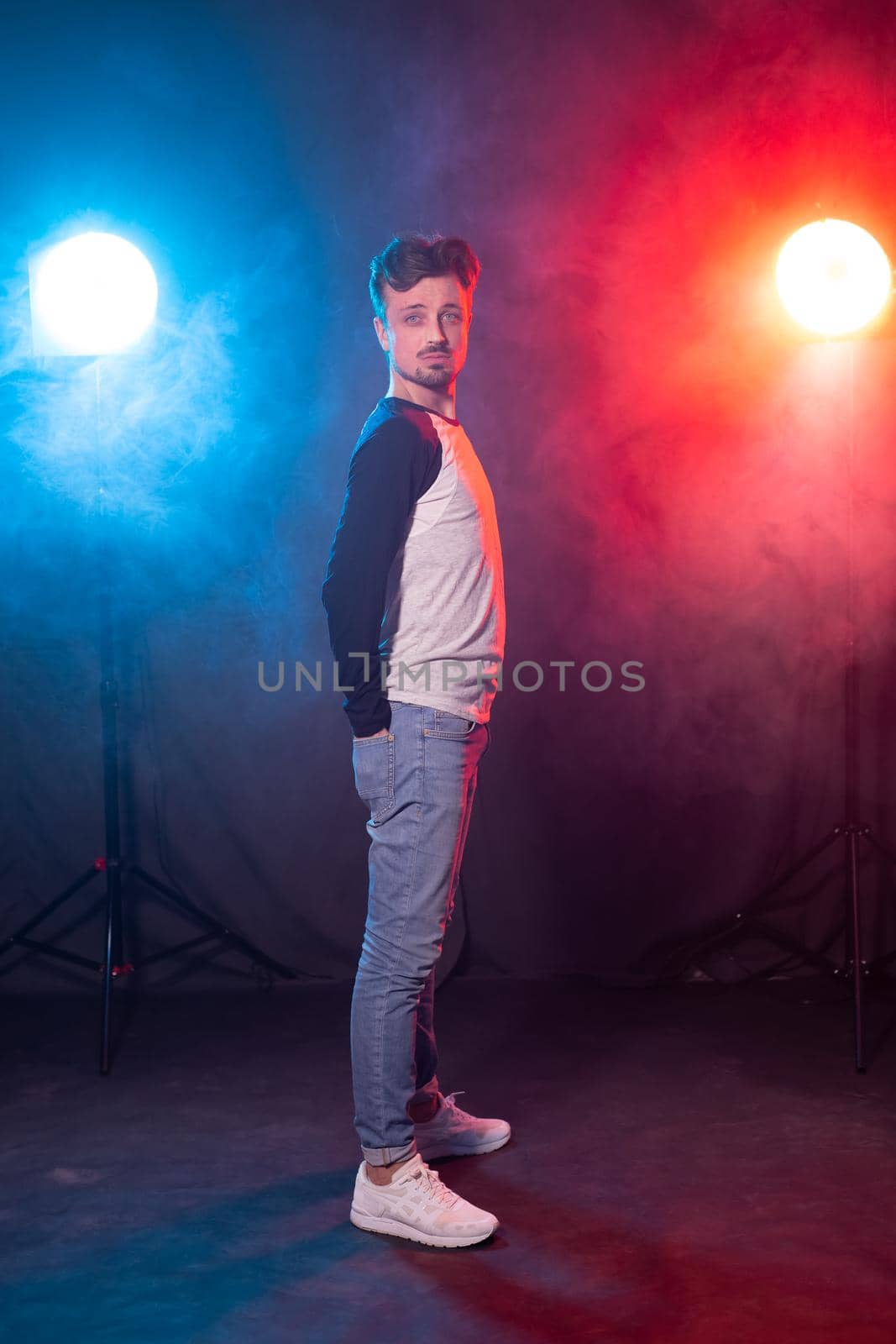 Slim young bearded hipster man in casual clothes posing on a red blue background. Concept of style and confidence