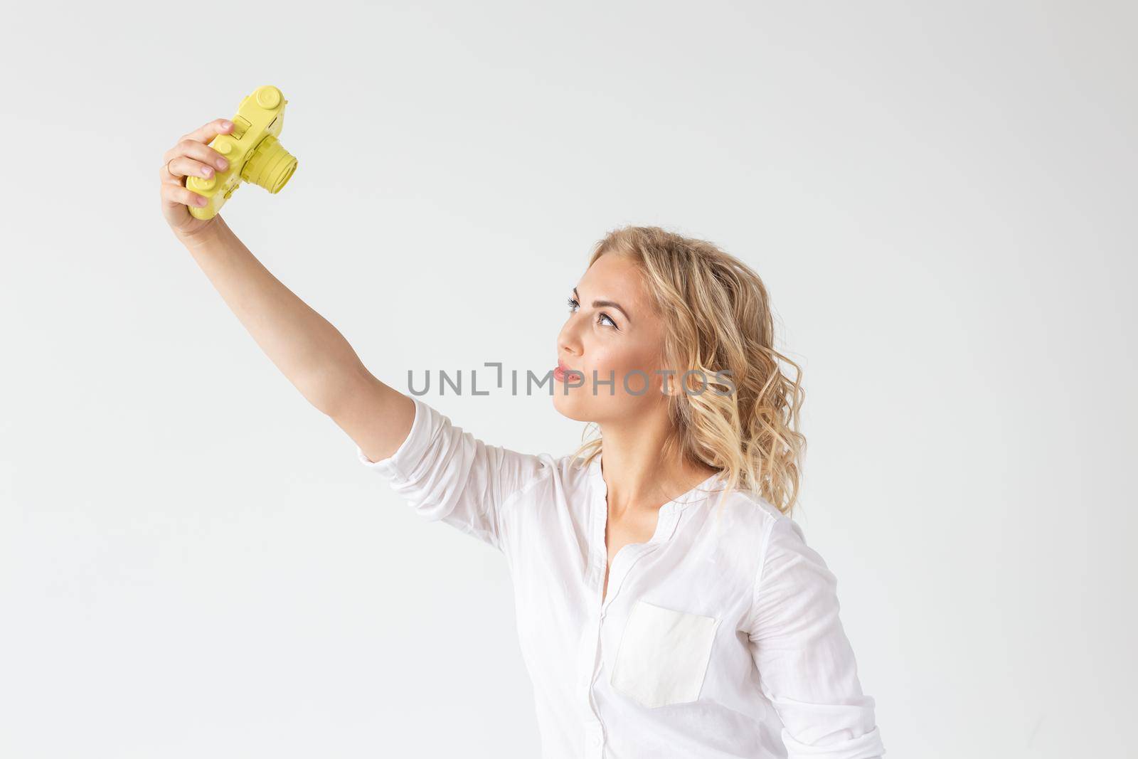 Smiling young woman is holding in her hands a yellow vintage camera model posing on a white background. Concept of amateur and professional photography