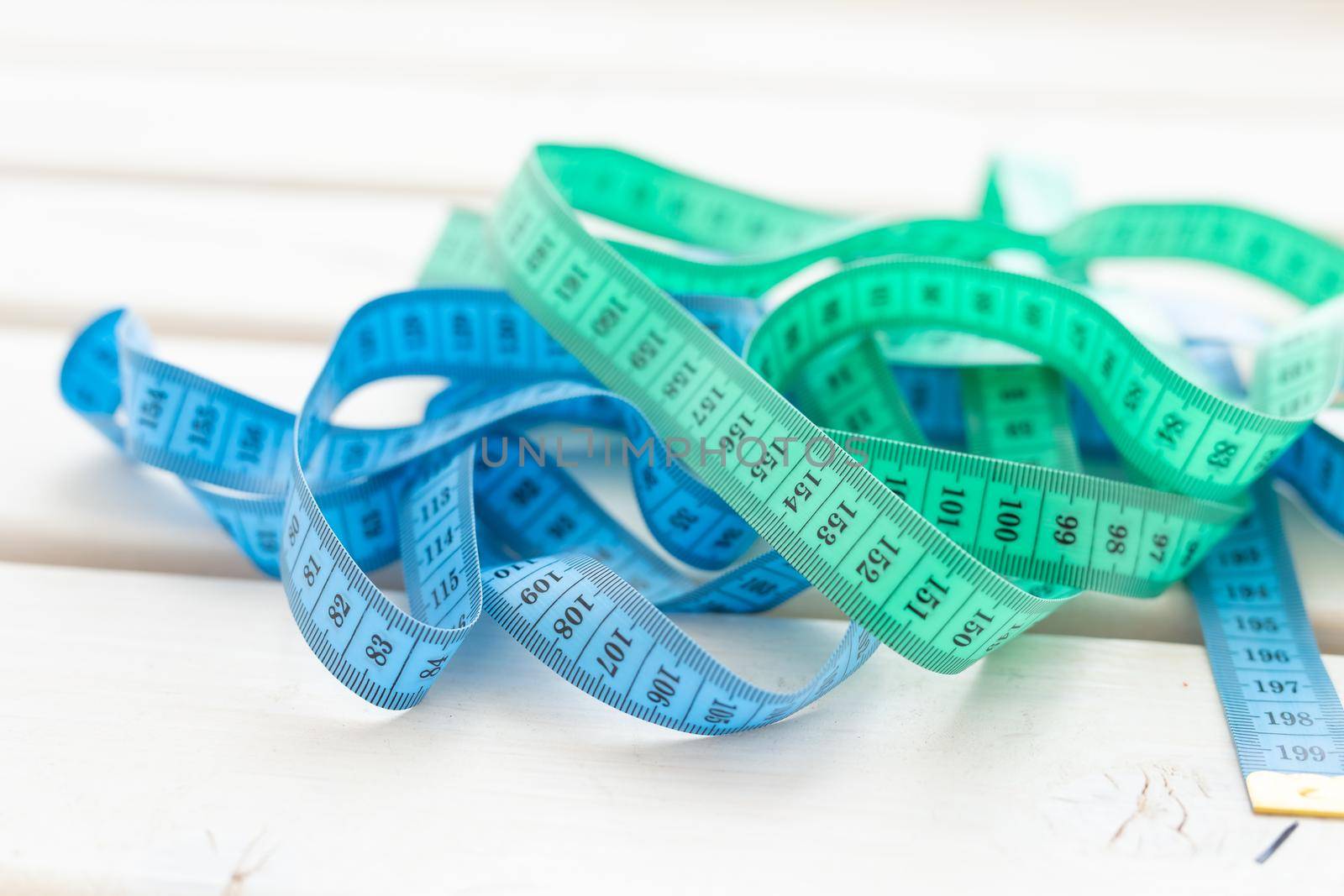 Close up blue and green measuring tape lying on the table. Concept measurement of healthy eating and weight loss by Satura86