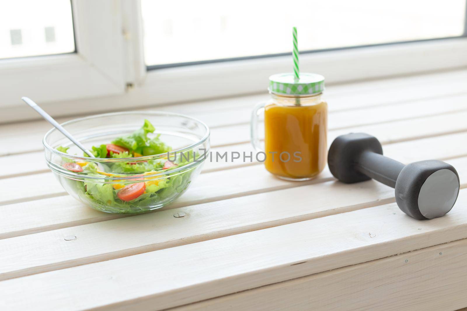 Vegetable salad fruit smoothies and dumbbell lie on a white windowsill. Concept of healthy lifestyle physical activity and proper nutrition. by Satura86