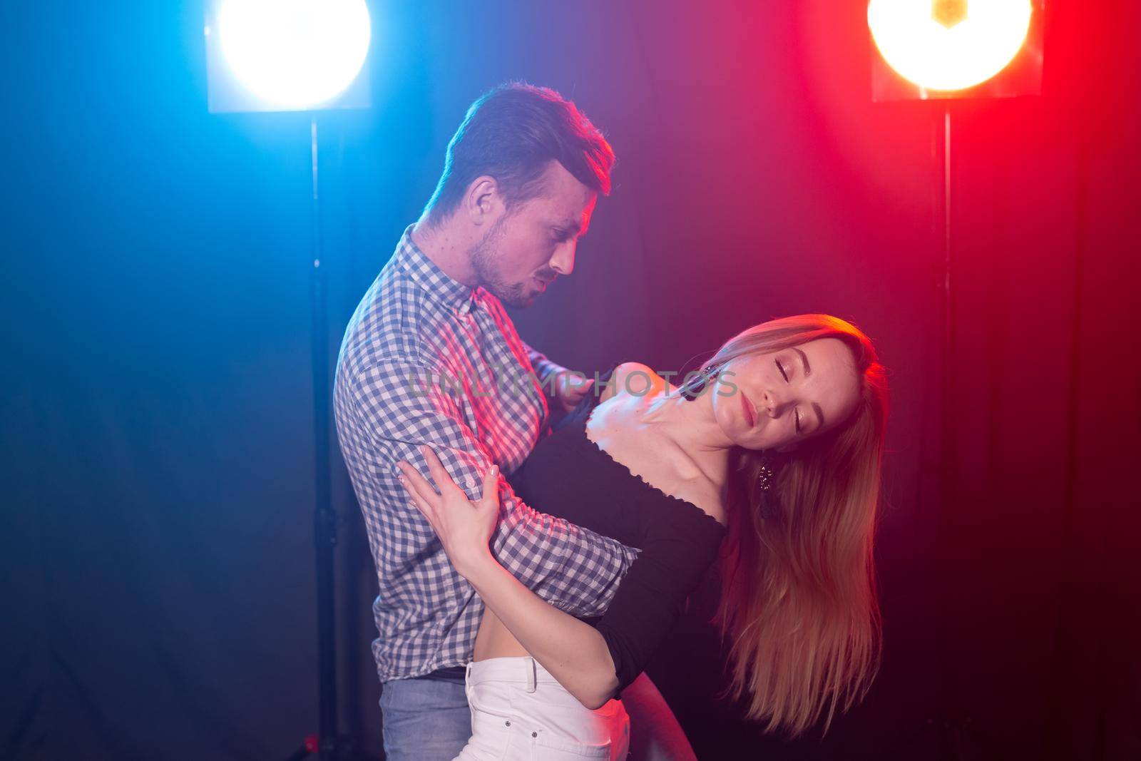 Social dance, bachata, kizomba, zouk, tango concept - Man hugs woman while dancing over lights.