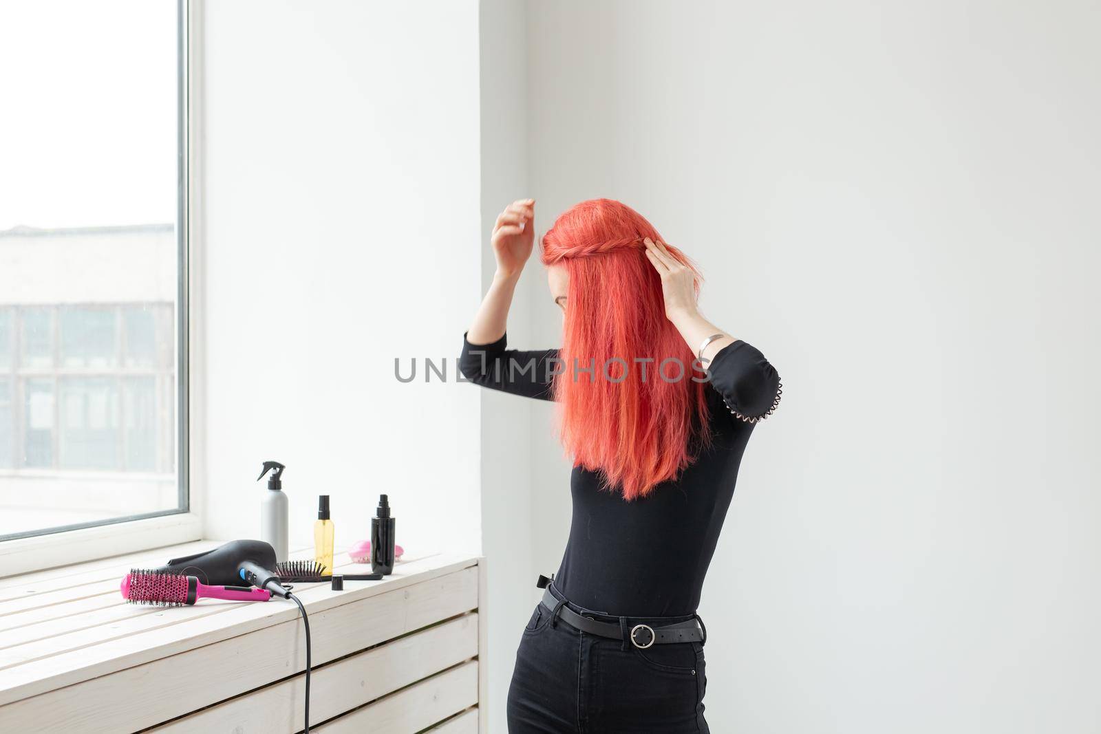 Beautiful red-haired girl with long hair, she is weaves a braid, in a beauty salon. Professional hair care and creating hairstyles