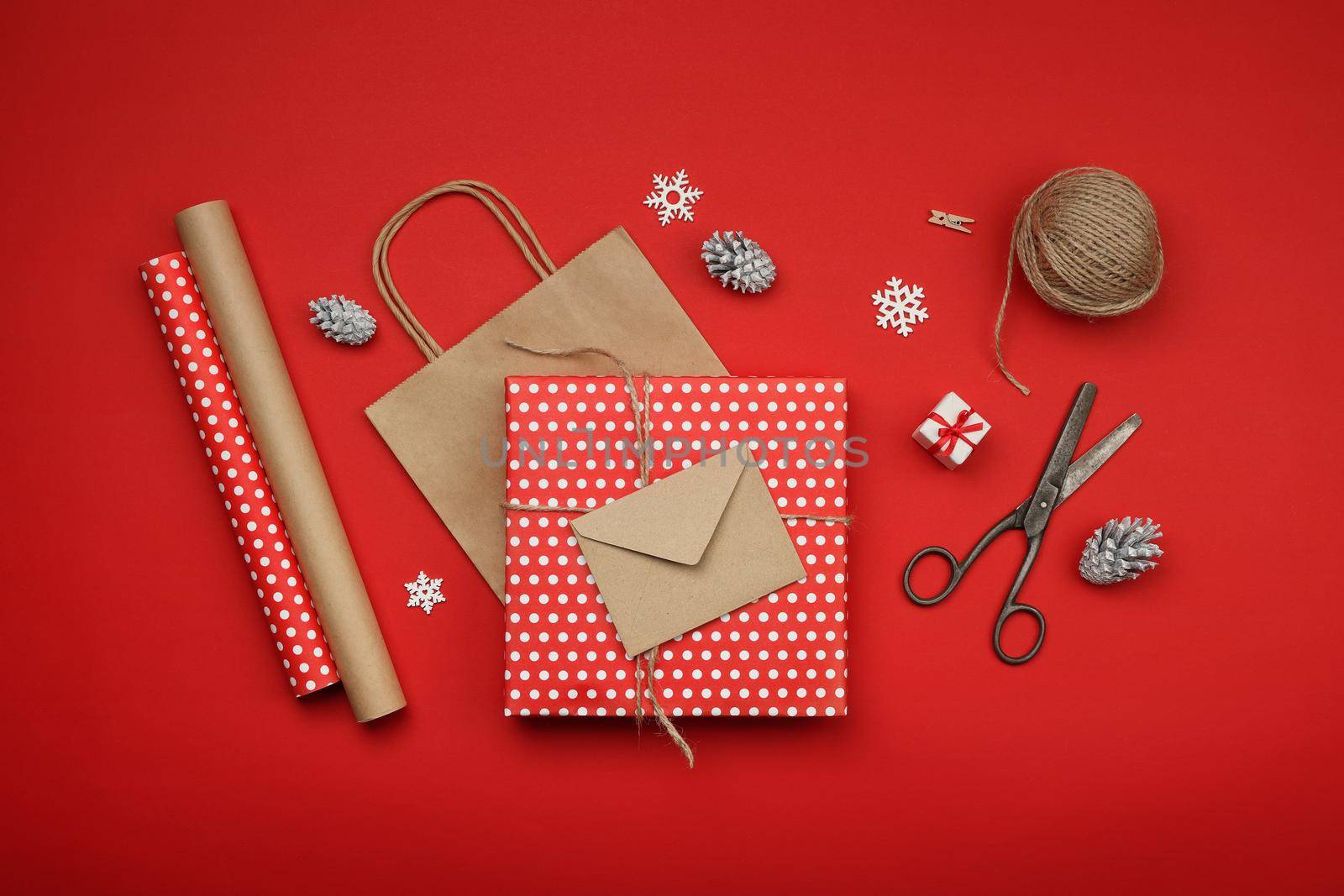 Close up packing and wrapping Christmas gifts with red and brown paper, table top view, flat lay