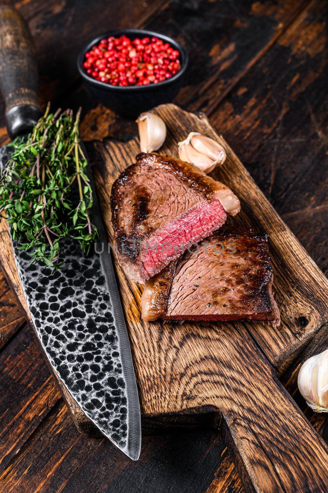 Cut fried rump cap or brazilian picanha beef meat steak on a wooden board. Dark wooden background. Top view.