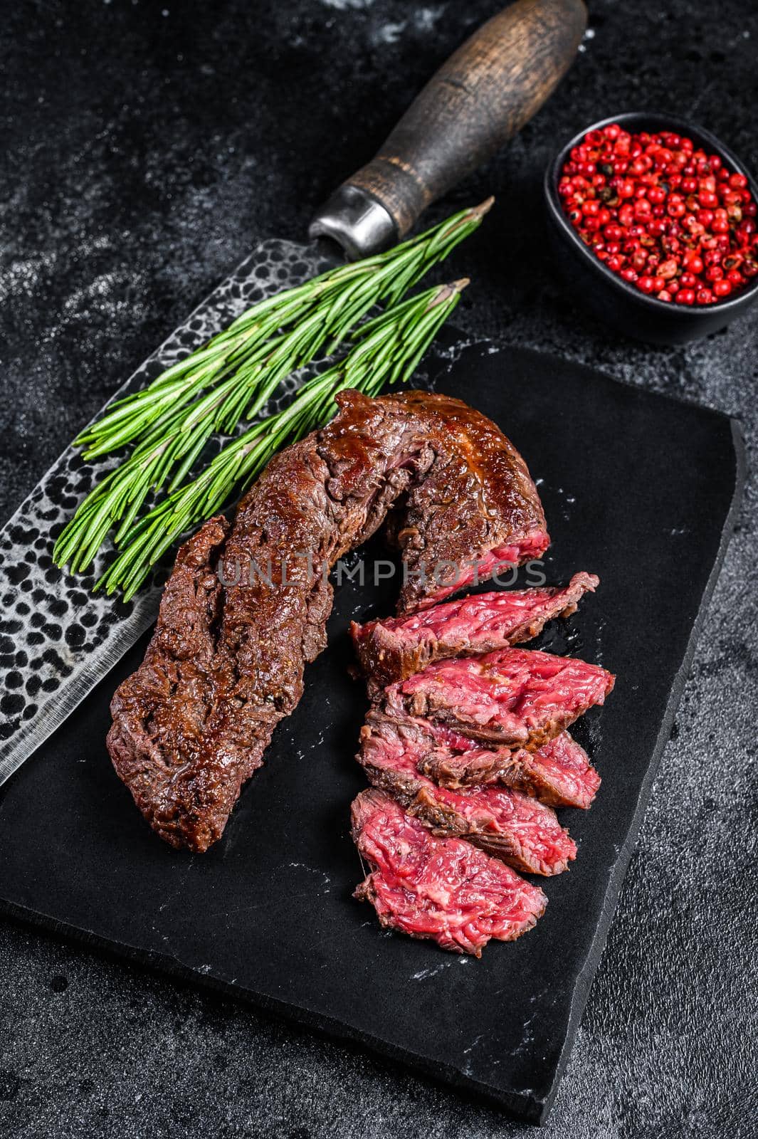 Sliced grilled Onglet Hanging Tender steak on a marble board. Black background. Top view.