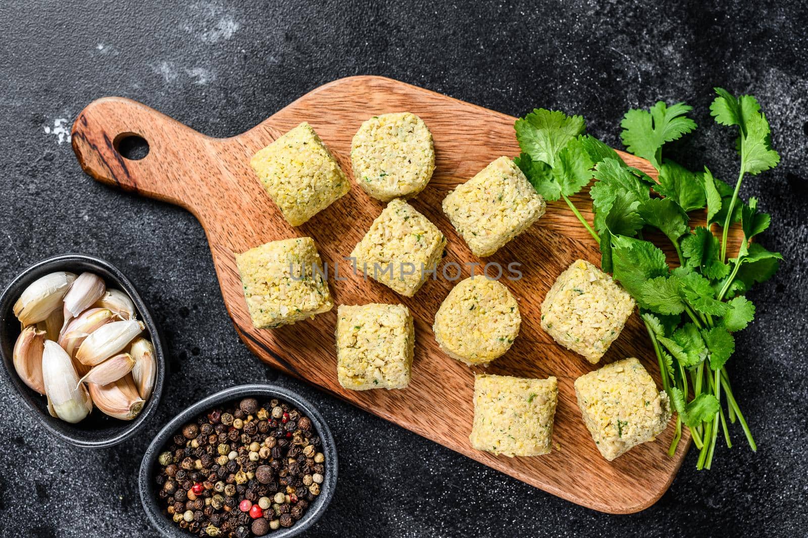 Raw falafel balls on a wooden cutting board. Black background. Top view.