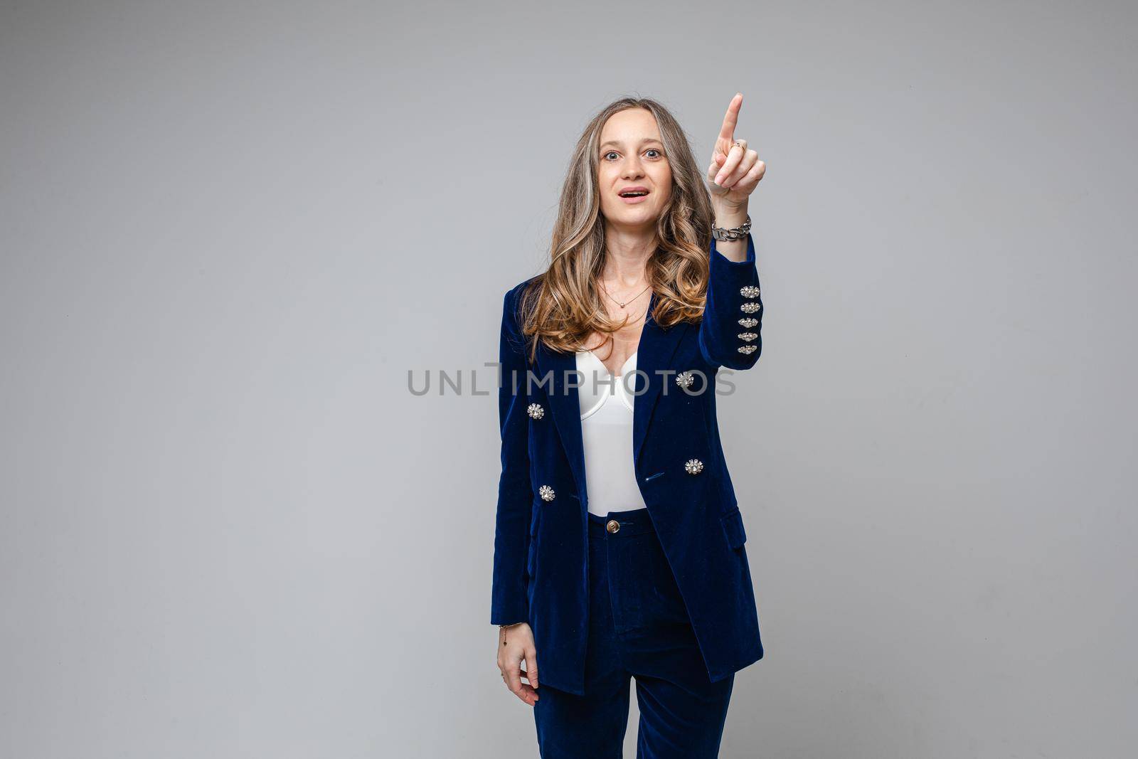 caucasian woman with attractive appearance points something her finger up, picture isolated on grey background