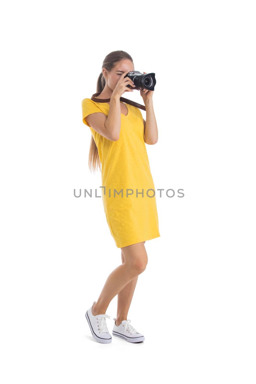 Young caucasian woman in yellow dress takes images with photo camera. Full length portrait. Isolated on the white background.