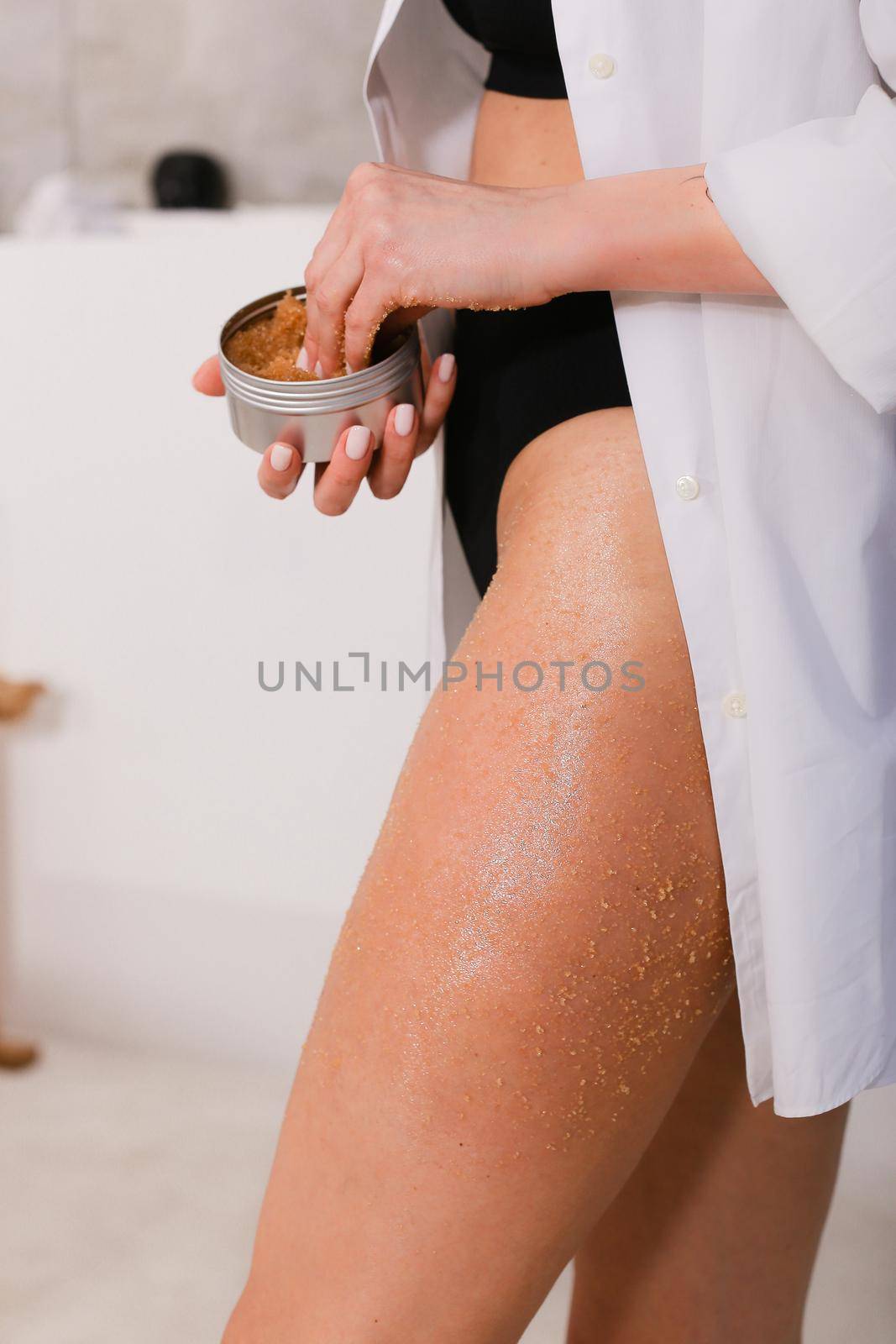 Woman applying nourishing scrub on body on bathroom background, closeup by sisterspro