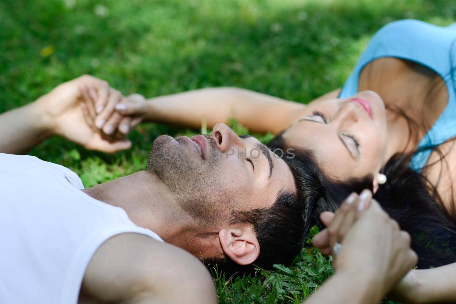 Happy smiling couple laying on green grass in a beautiful park