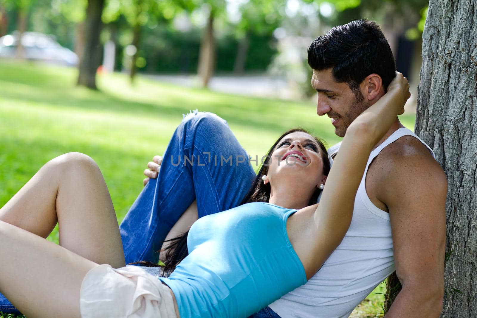 Happy smiling couple laying on green grass in a beautiful park