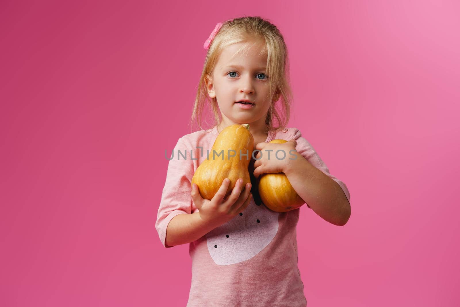 Little girl holding pumpkin in her hands against pink background by Fabrikasimf