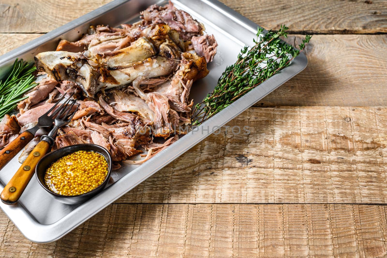 Roast pork knuckle eisbein meat on a baking pan with herbs. Wooden background. Top view. Copy space.