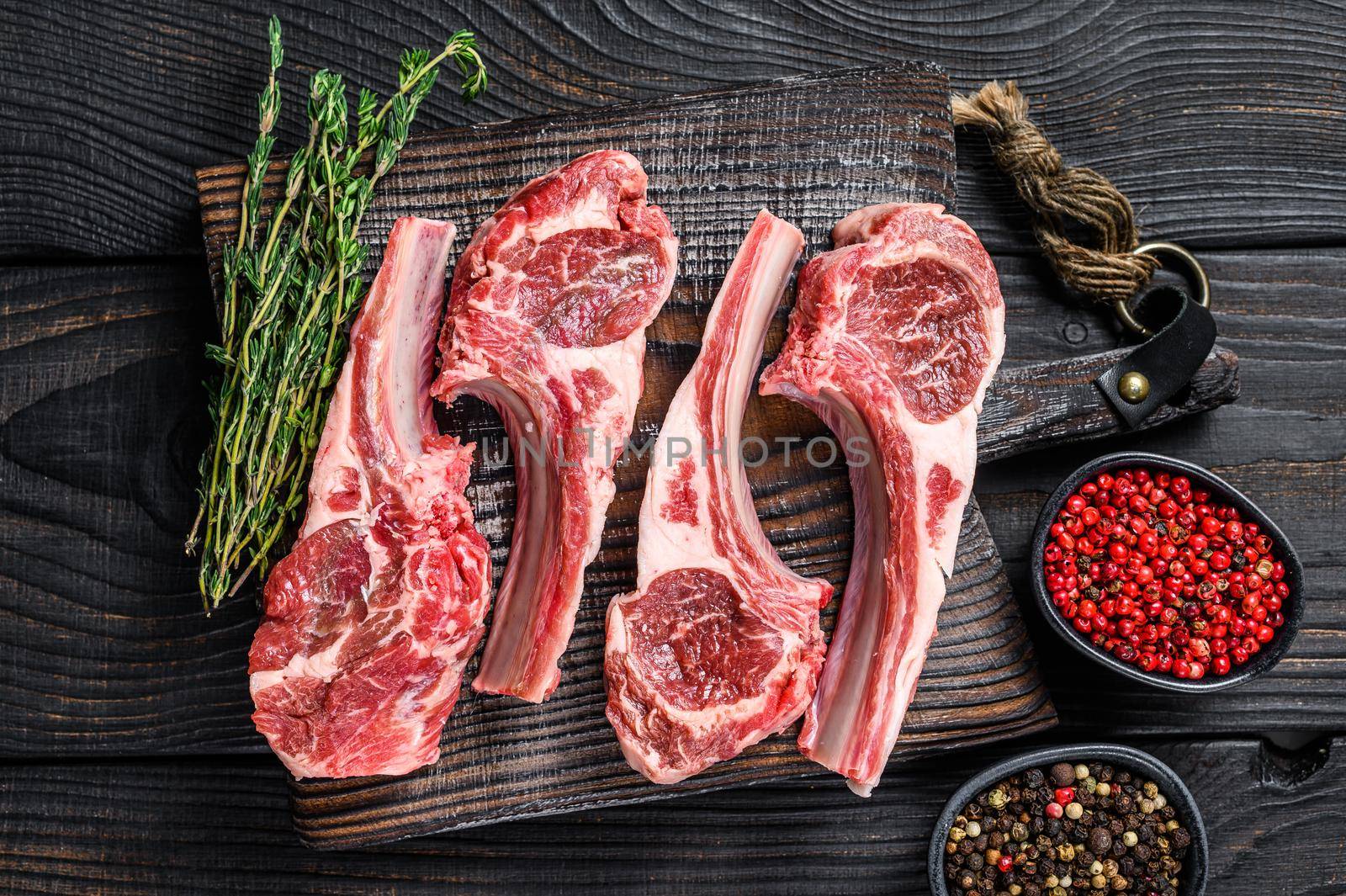 Lamb chops raw meat on bone with salt, pepper and herbs. Black wooden background. Top view.