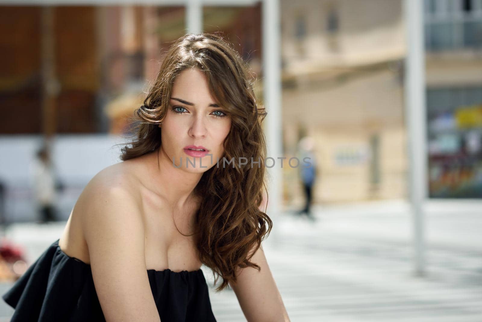 Beautiful young woman with blue eyes and long hair in urban background. Girl wearing summer clothes. Curly hairstyle.