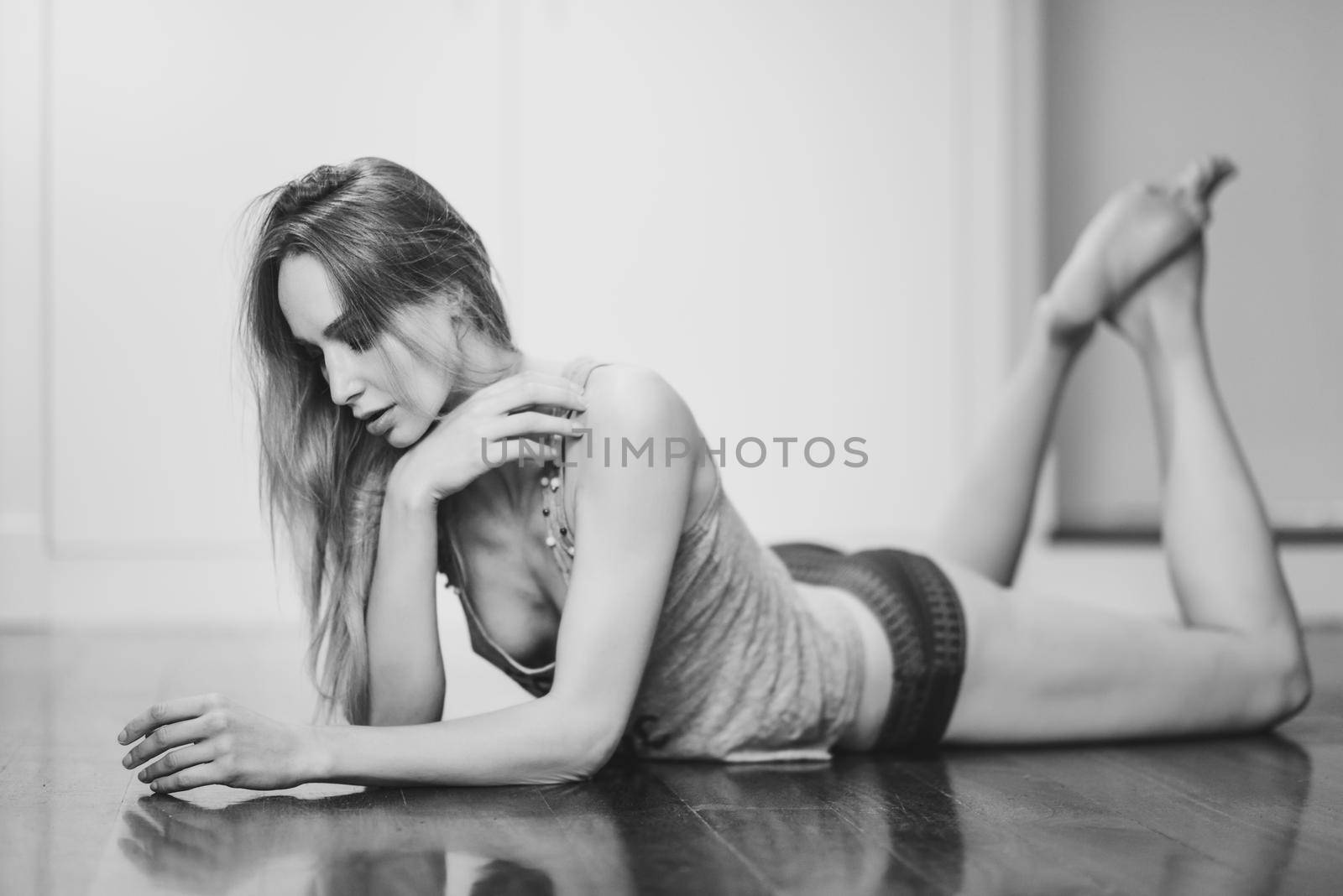 Beautiful blonde woman in white lingerie laying on wooden floor. Young girl wearing underwear with long hair. Female wearing t-shirt and red panties.