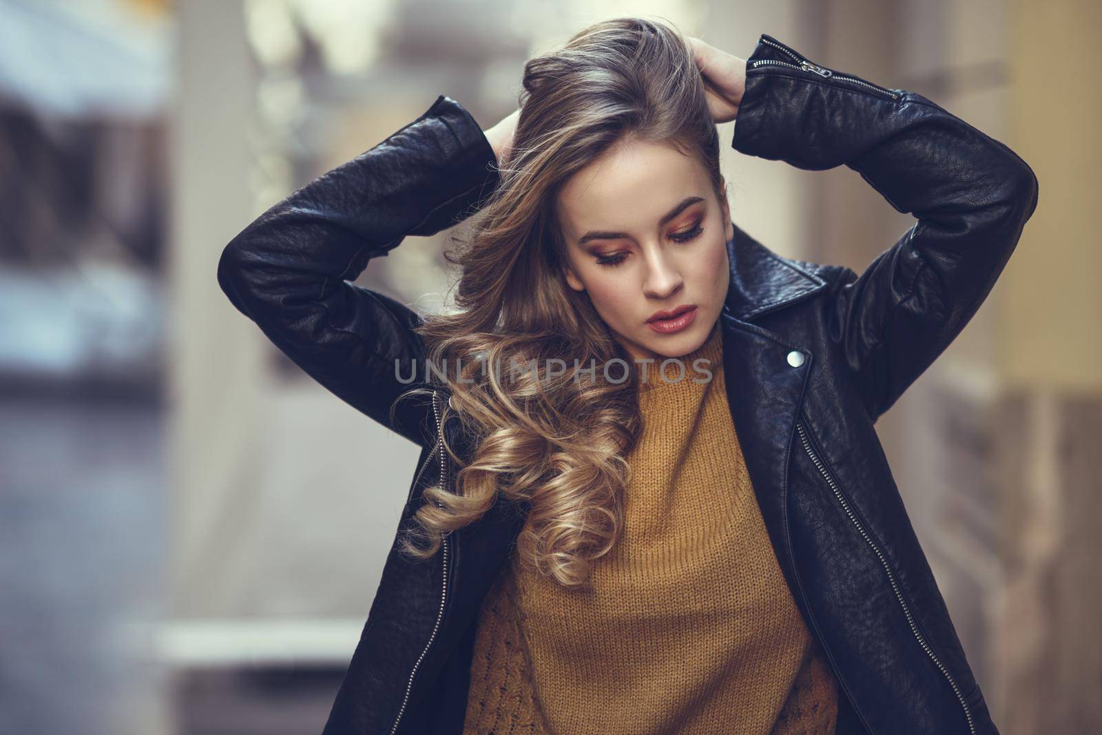 Blonde woman in urban background. Beautiful young girl wearing black leather jacket and mini skirt standing in the street. Pretty russian female with long wavy hair hairstyle and blue eyes.