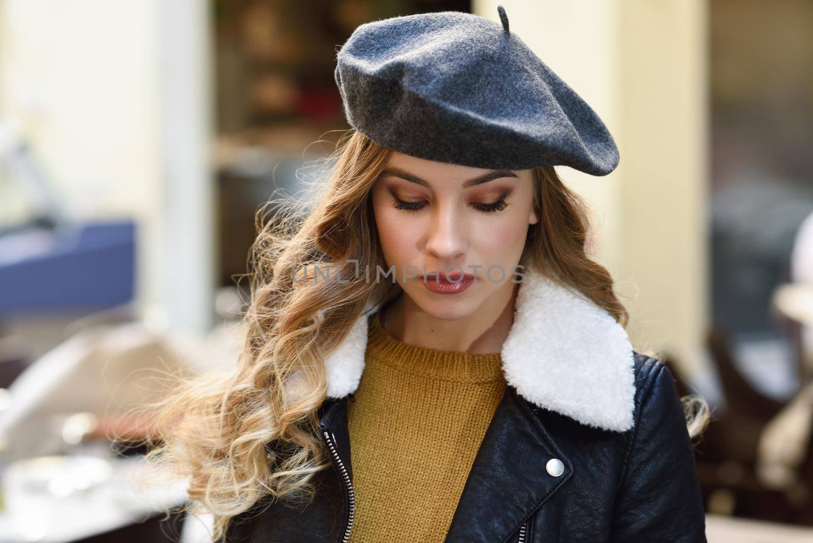 Blonde russian woman in urban background. Beautiful young girl wearing beret, black leather jacket and mini skirt standing in the street. Pretty female with long wavy hair hairstyle.