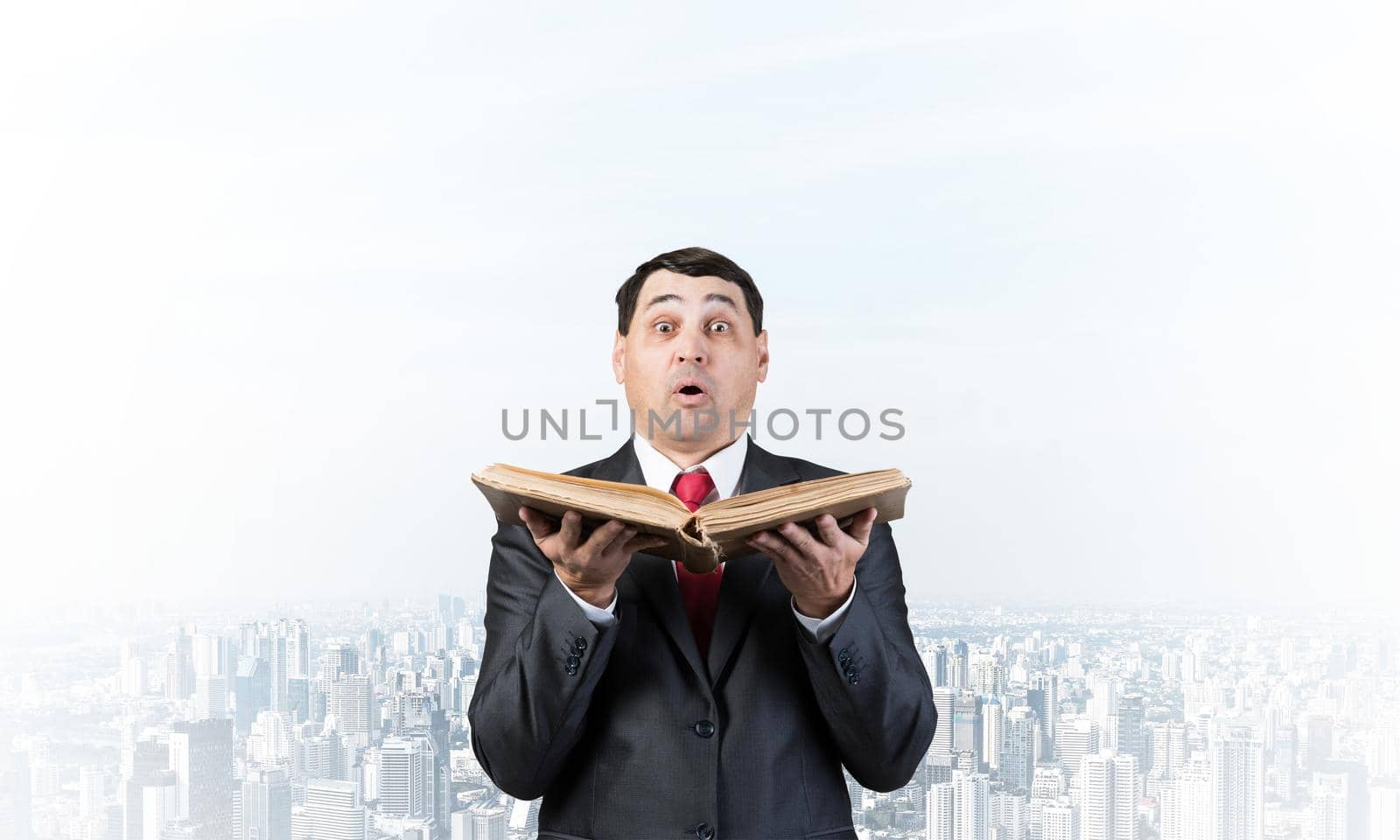 Surprised businessman holding open old book. Startled adult man in business suit and tie standing on downtown background. Business education and knowledges. Business paperwork and bookkeeping concept.