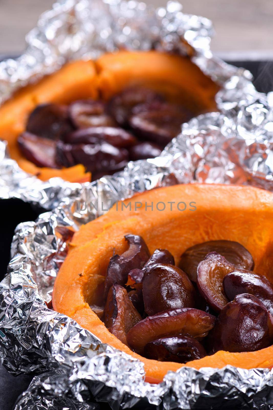 Hokkaido pumpkin halves baked in foil stuffed with plums on a baking sheet. Vegetarian food. The ketogenic diet. Vegan paleo