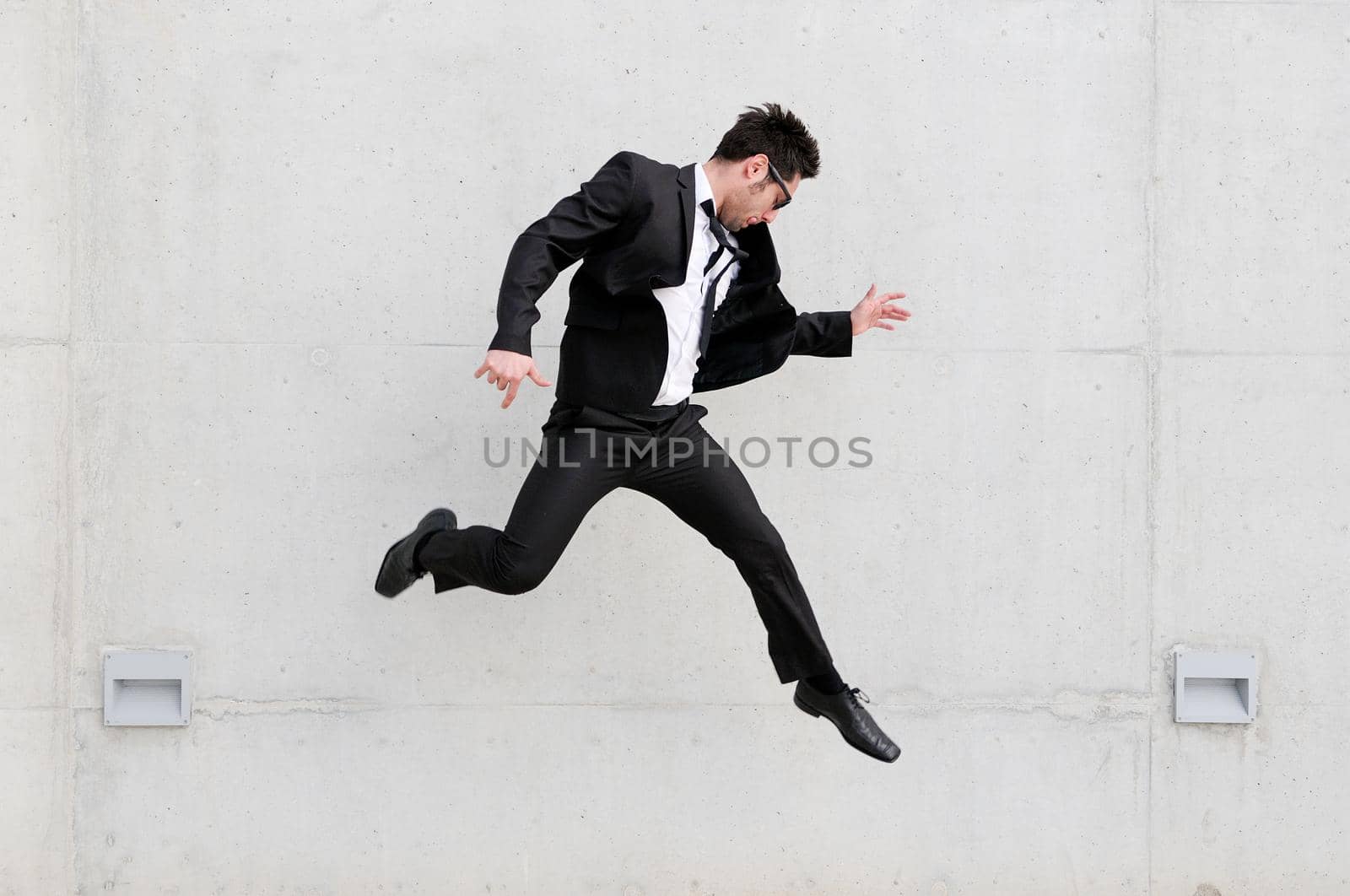 Young handsome businessman with eyeglasses jumping in the street