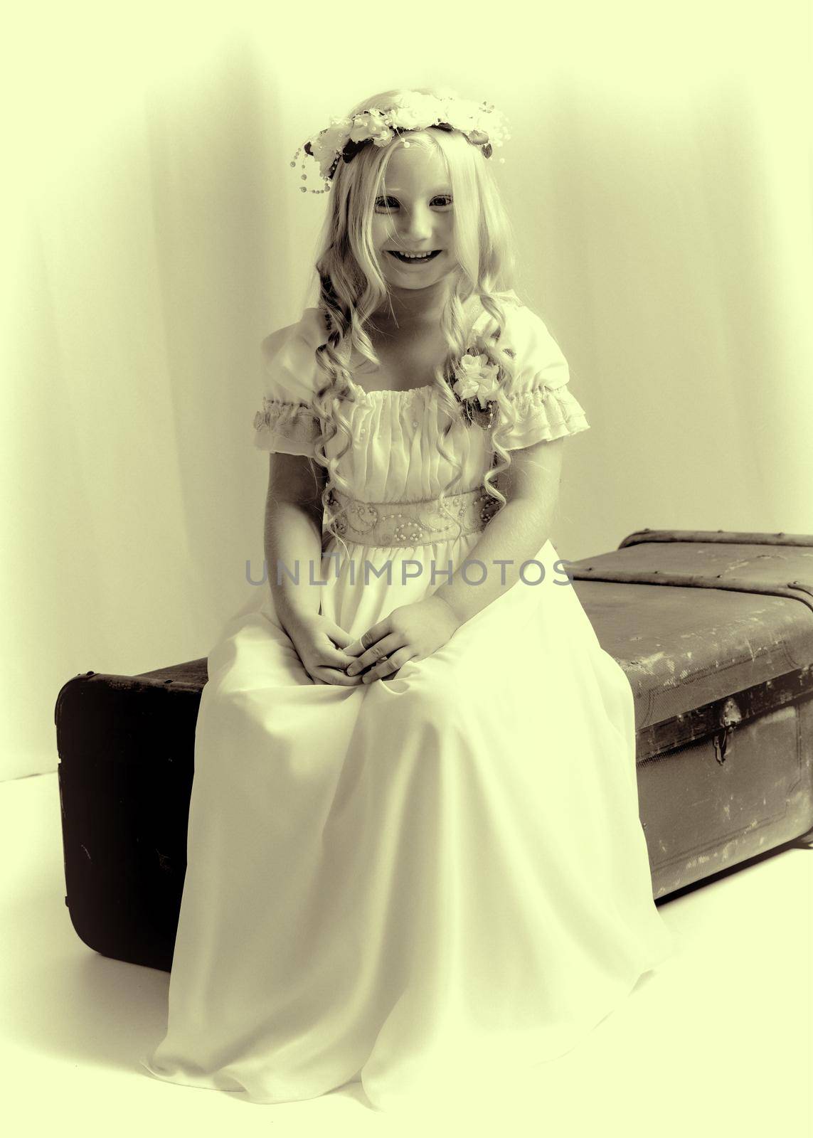 A nice little girl is sitting on an old suitcase. Retro style.