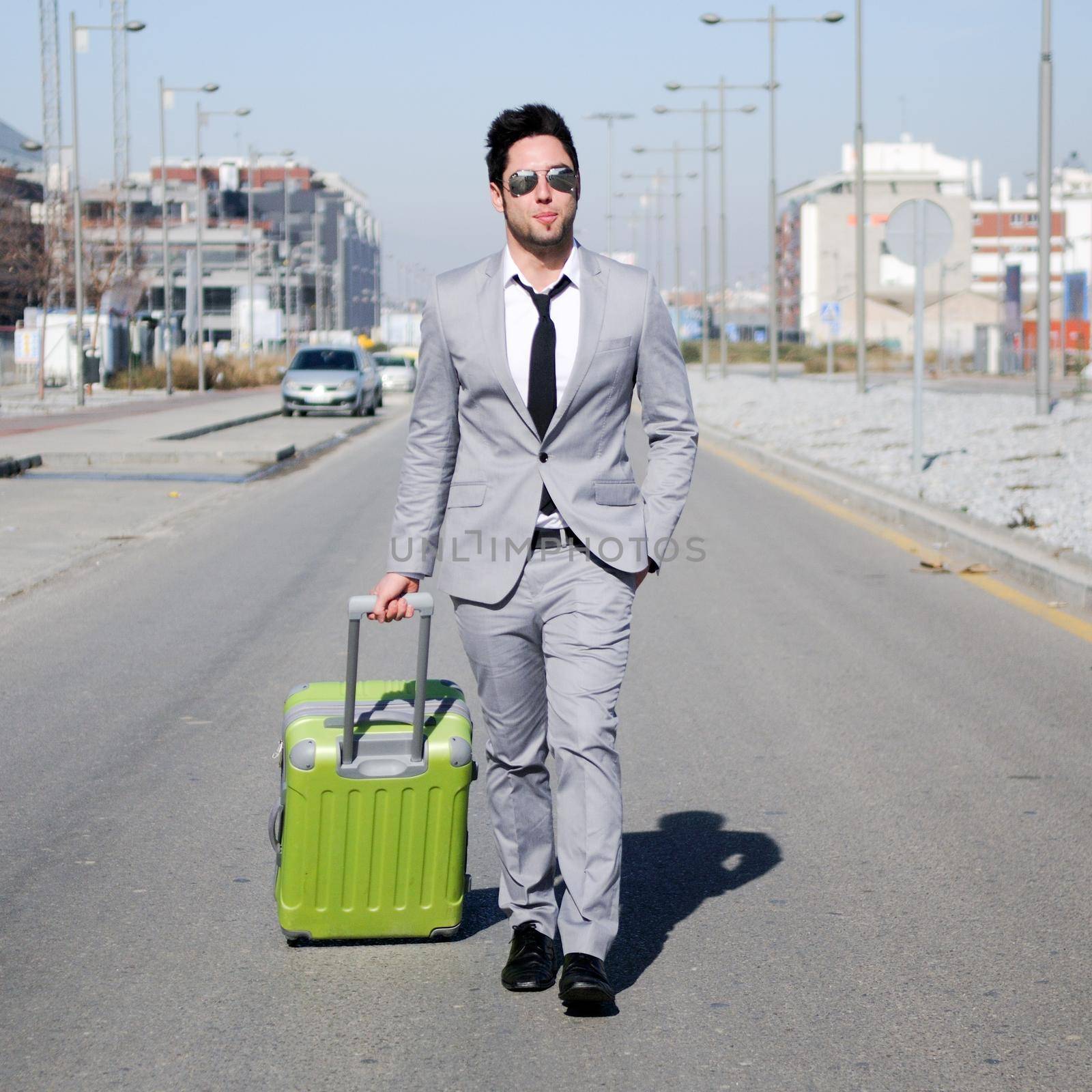 Man dressed in suit and suitcase walking along the street by javiindy