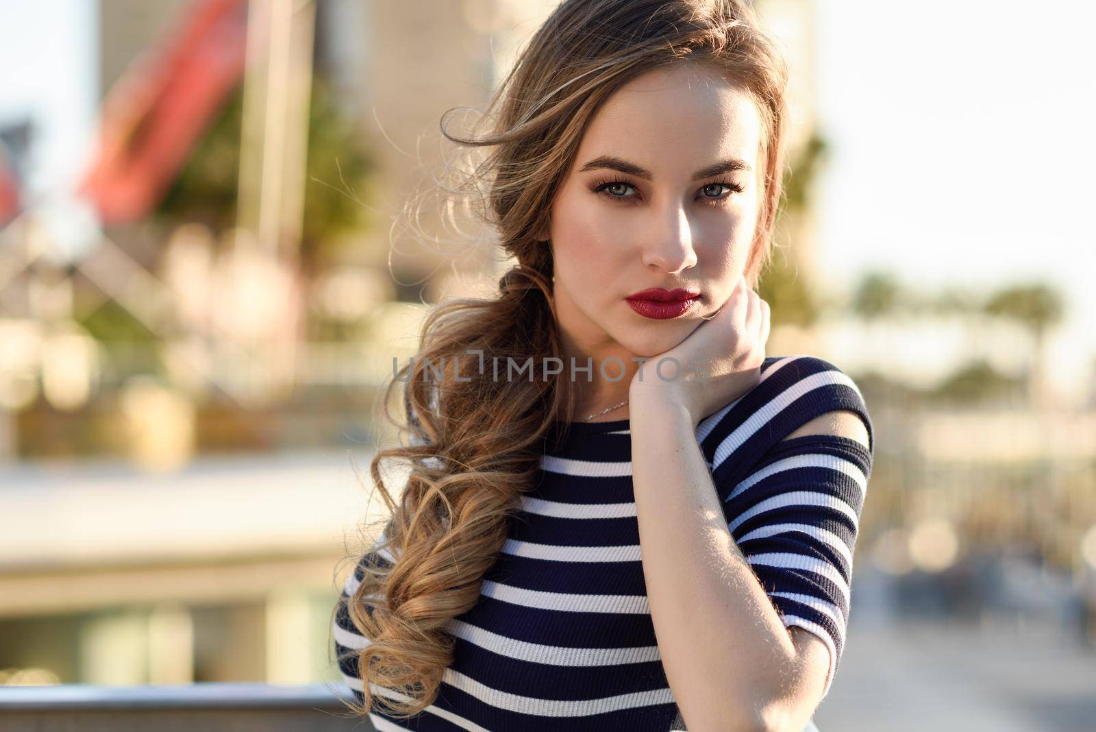 Blonde woman, model of fashion, standing in urban background. Beautiful young girl wearing striped t-shirt and blue jeans in the street. Pretty russian female with pigtai and blue eyes.