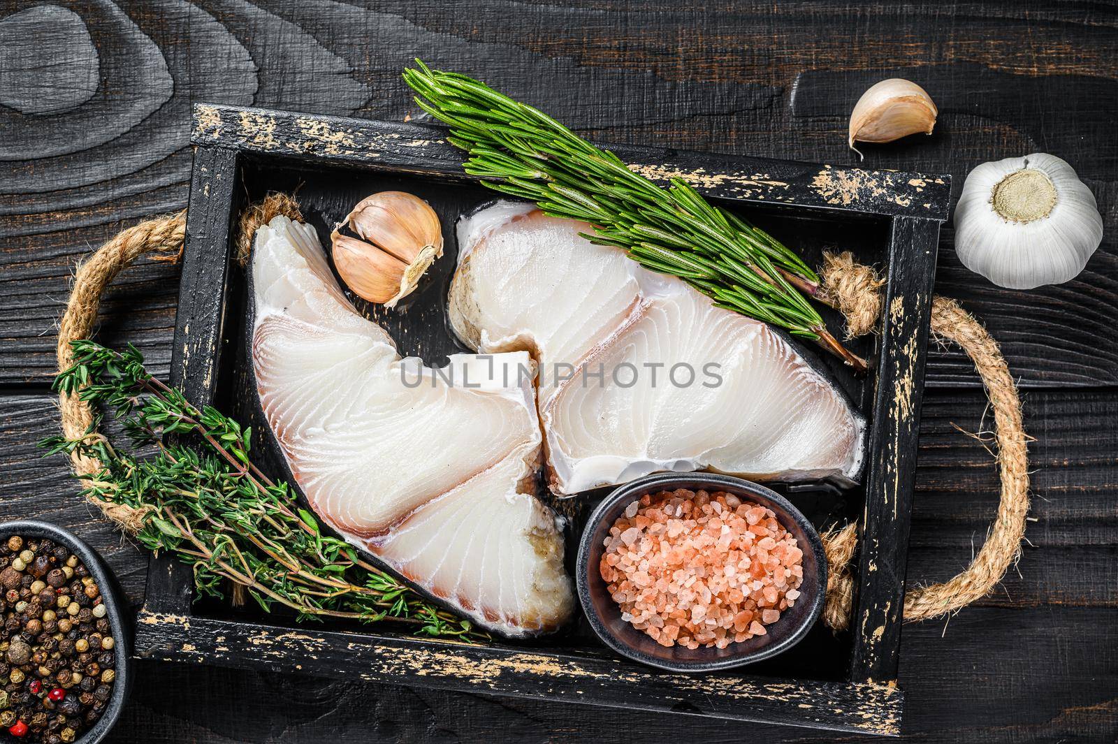 Shark raw fish steaks in a wooden tray with herbs. Black wooden background. Top view.