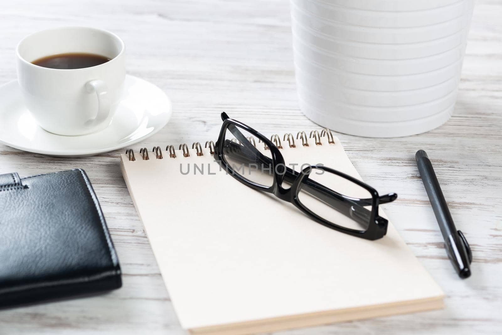 Top view office desk with white cup of coffee. Flat lay vintage wooden table with spiral notebook, glasses and pen. Coffee break time. Corporate business concept. Relax at work with hot drink.