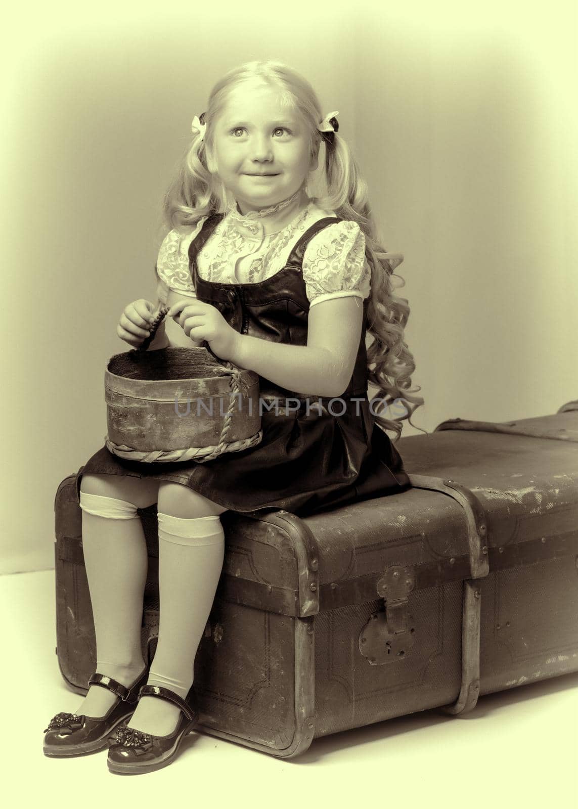A little girl is sitting on an old suitcase with a basket. by kolesnikov_studio