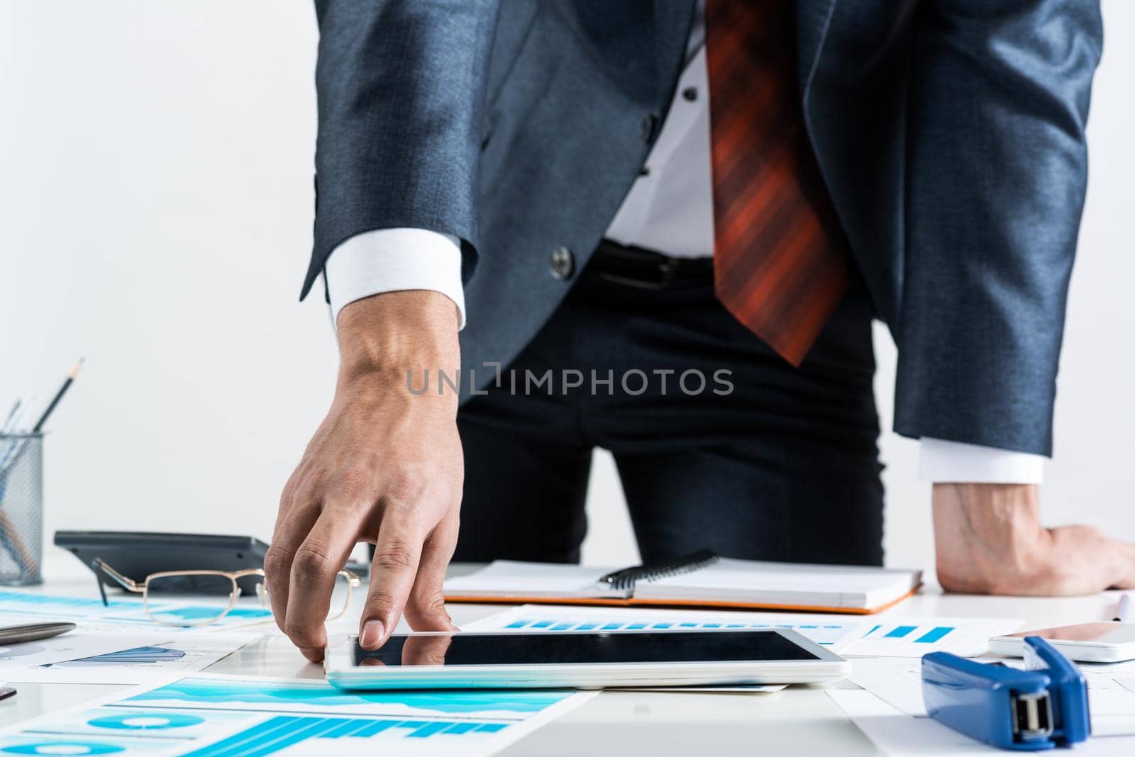 Businessman standing near office desk and using tablet computer. Banking and financial management. Corporate manager in suit and tie working with business analytics. Entrepreneurship and leadership.