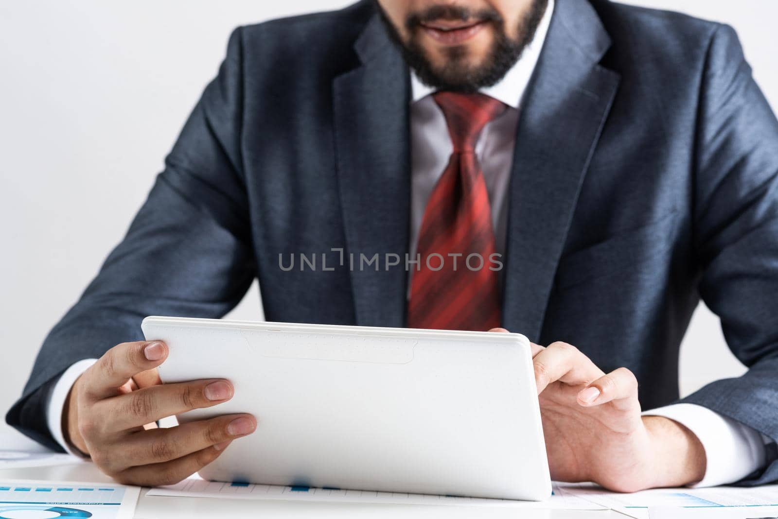 Businessman using tablet computer at office desk. Financial expertise and consulting. Manager in suit and tie sitting at desk with documents and tablet computer. Corporate accounting and paperwork