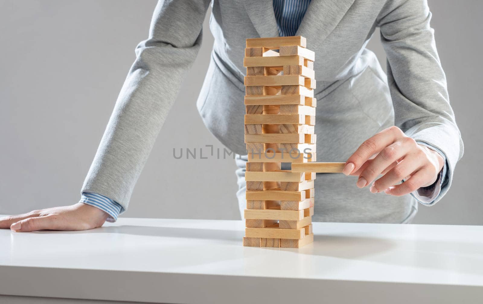 Businesswoman removing wooden block from tower on table. Management of risks concept with wooden boxes game. Business development and assistance. New challenge and leadership motivation.