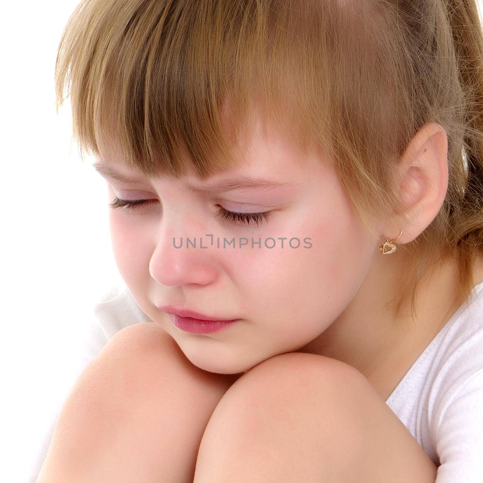 A sweet little gymnast girl is upset, she sits on the floor and cries. The concept of sport, children's emotions. Isolated on white background.