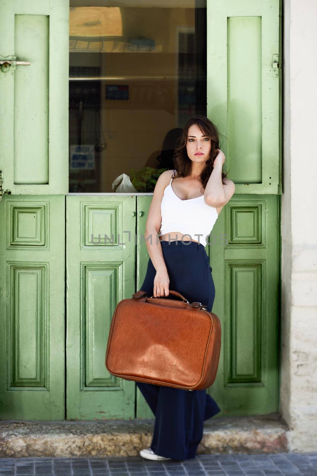 Beautiful girl with vintage bag against green door by javiindy