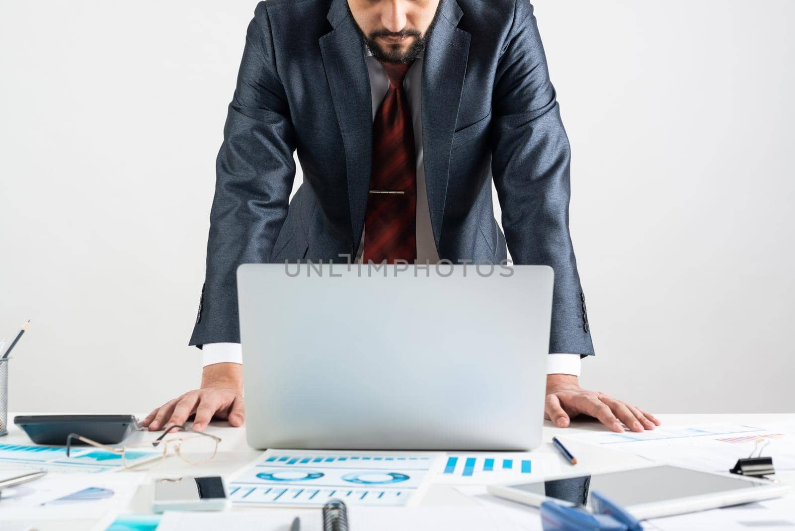 Businessman in suit and tie standing near office desk with documents and laptop. Meeting in conference room. Business idea presentation, analyze and strategy planning. Entrepreneurship and leadership