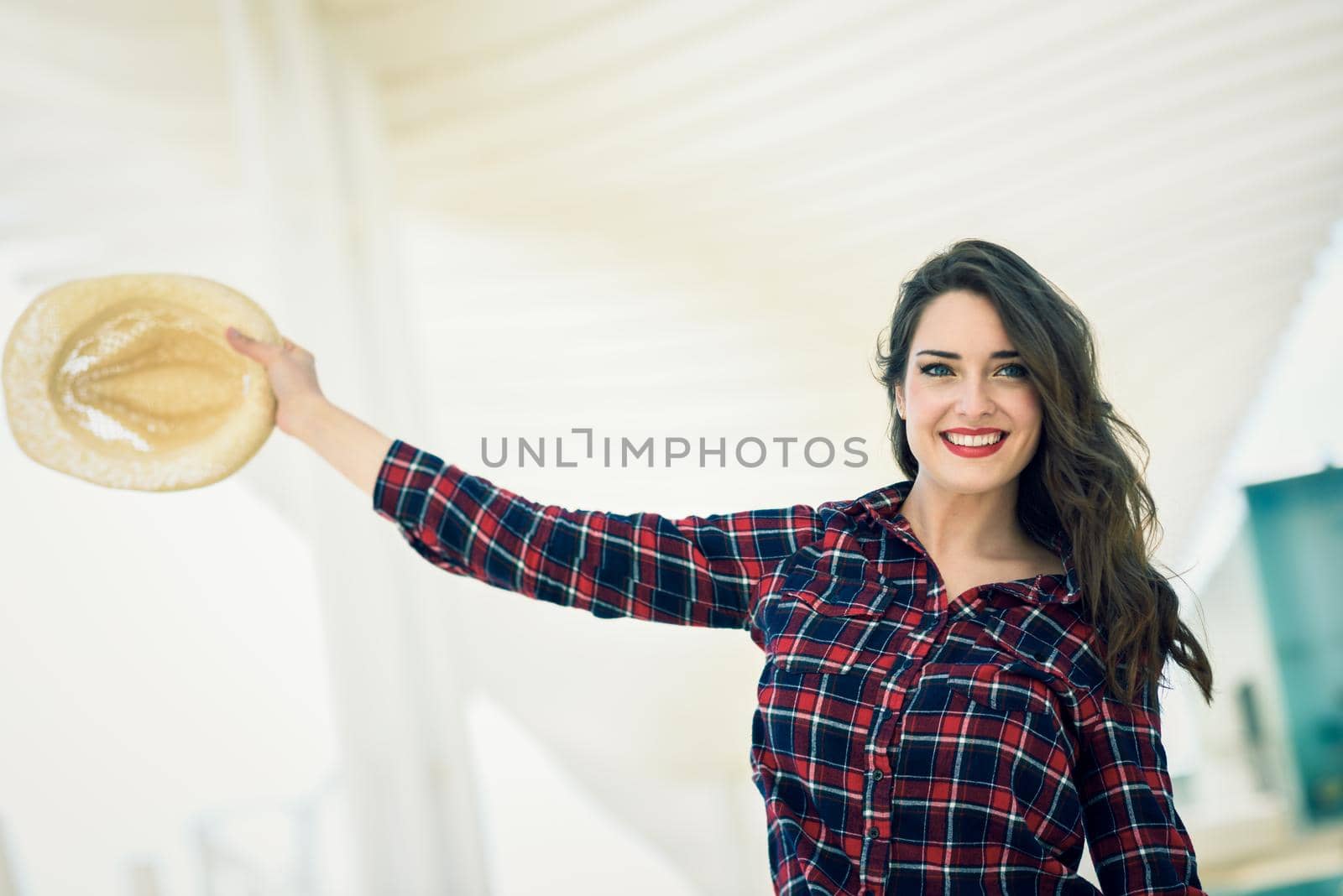 Young woman with beautiful blue eyes wearing plaid shirt and sun hat. Girl smiling in urban background.
