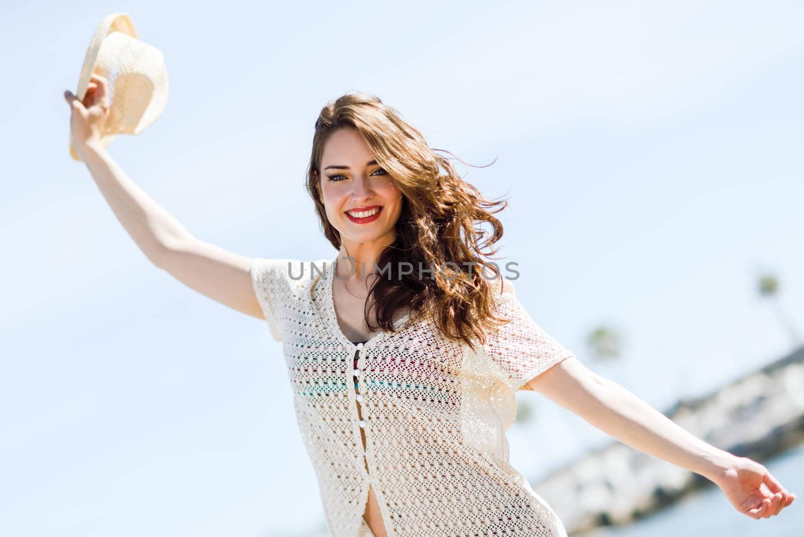 Beautiful young woman with open arms smiling in the beach.